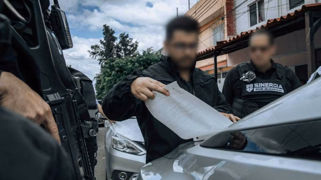 agente-de-la-fiscalia-de-queretaro-revisa-un-documento-sobre-el-cofre-de-un-vehiculo-junto-a-elementos-de-sinergia-por-queretaro